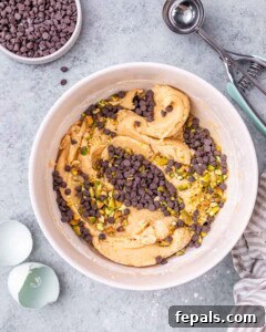 Cookie dough in a mixing bowl, now mixed and topped with mini chocolate chips and finely chopped roasted pistachios.