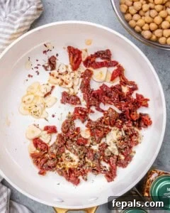 Garlic slices, chopped sun dried tomatoes, and seasonings sizzling in oil in a pan.