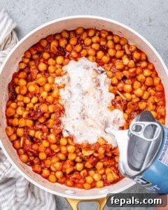 Coconut cream poured over chickpeas and tomato sauce in a pan.