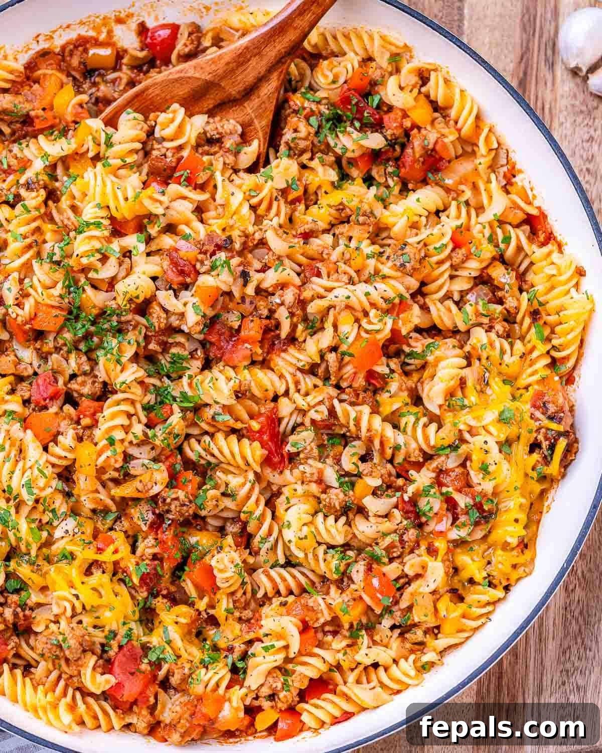 A skillet full of golden, cheesy ground turkey pasta, showcasing the mix of pasta, turkey, and colorful peppers.