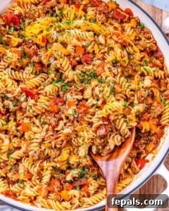 Comforting Ground Turkey Pasta 12 Overhead view of a large skillet filled with cheesy ground turkey pasta, garnished with fresh herbs and served with a wooden spoon.