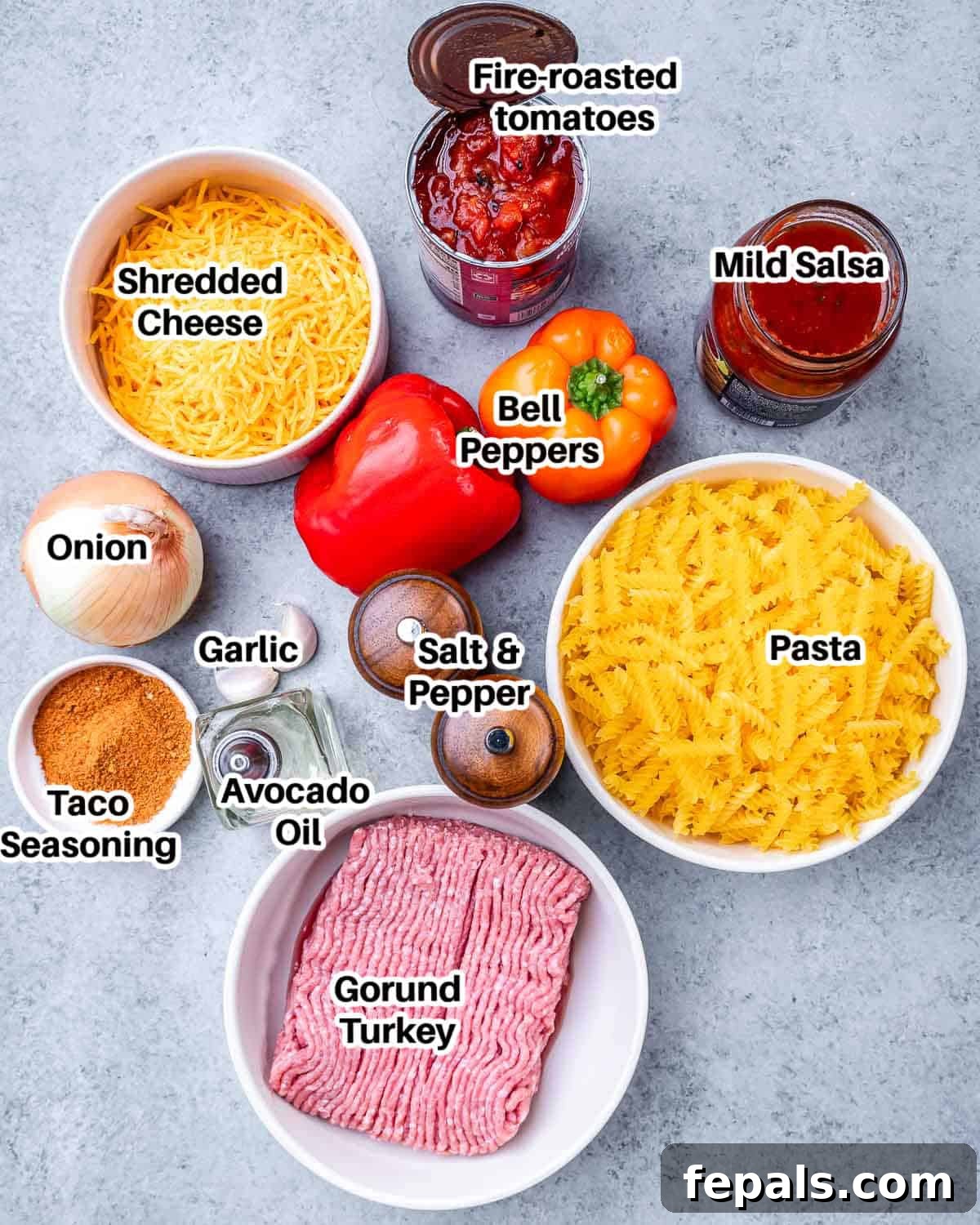 A flat lay of ingredients laid out on a white surface, including ground turkey, pasta, bell peppers, onions, garlic, taco seasoning, salsa, and fire-roasted tomatoes.