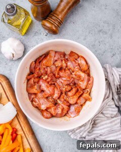 Raw sliced chicken marinating in seasoning inside a white bowl on a countertop.