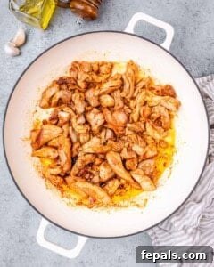 Cooked chicken pieces browning in a skillet with oil and seasoning.