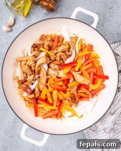Sautéed chicken added to a plate with sliced red and orange bell peppers.