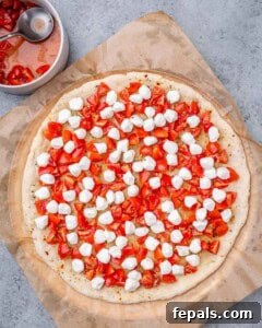 Pizza crust topped with mozzarella pearls and diced tomatoes, ready to bake.