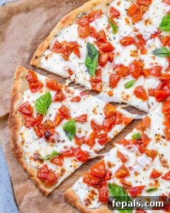 Whole baked bruschetta pizza topped with melted mozzarella, tomatoes, and fresh basil, centered in frame.