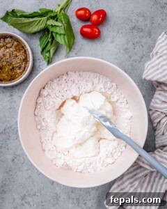 Mixing bowl filled with flour and yogurt being stirred with a spatula on a gray surface.