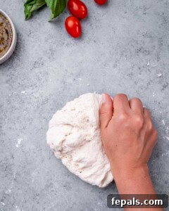 Hand kneading pizza dough on a lightly floured surface.