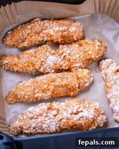 Breaded but uncooked chicken tenders on parchment paper, arranged in a single layer and ready for the air fryer.