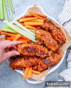 Fully cooked buffalo chicken tenders served in a bowl with fresh celery and carrot sticks, hand reaching in to grab one.
