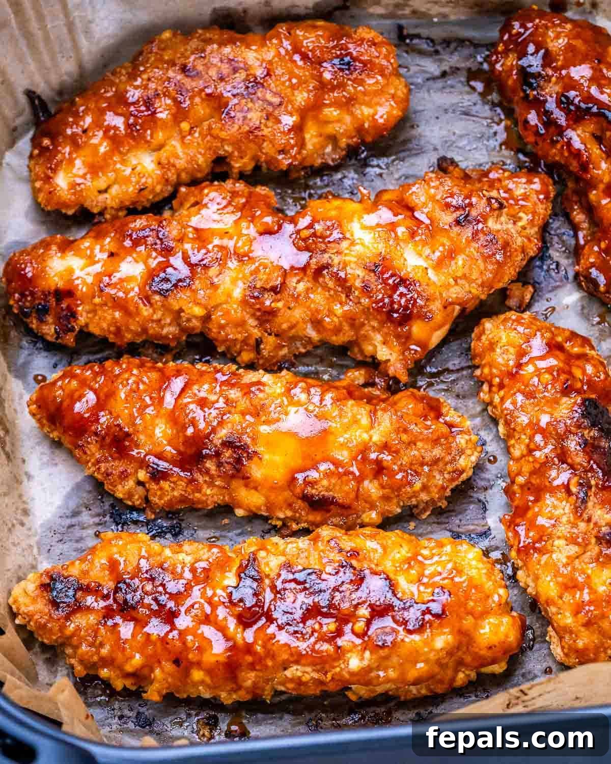 Zesty Air Fried Buffalo Chicken Strips 8 Crispy buffalo chicken tenders on parchment paper freshly cooked.