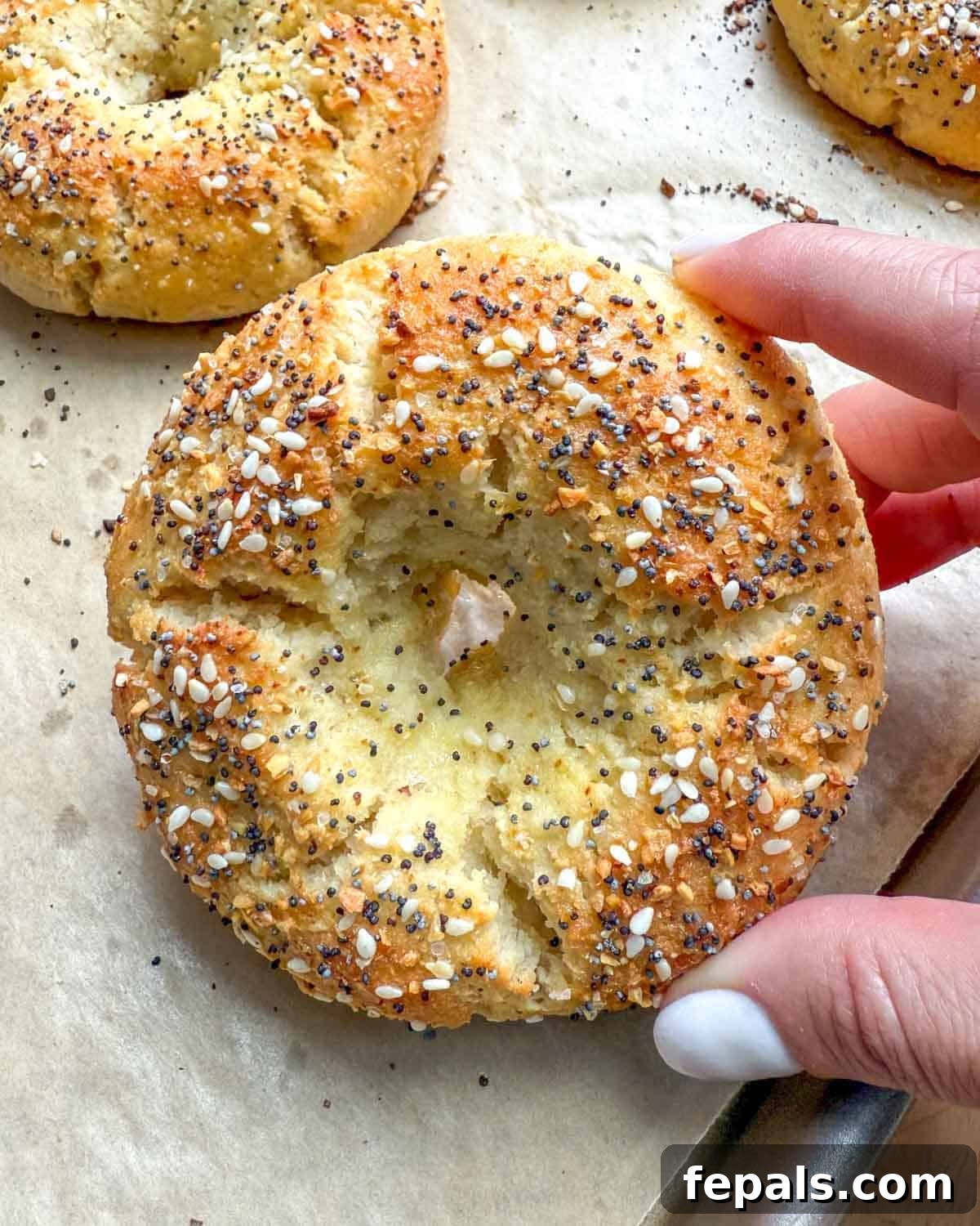 Low-Carb Almond Bagels 2 Hand holding up a single almond flour bagel, showcasing its golden-brown crust and inviting texture.