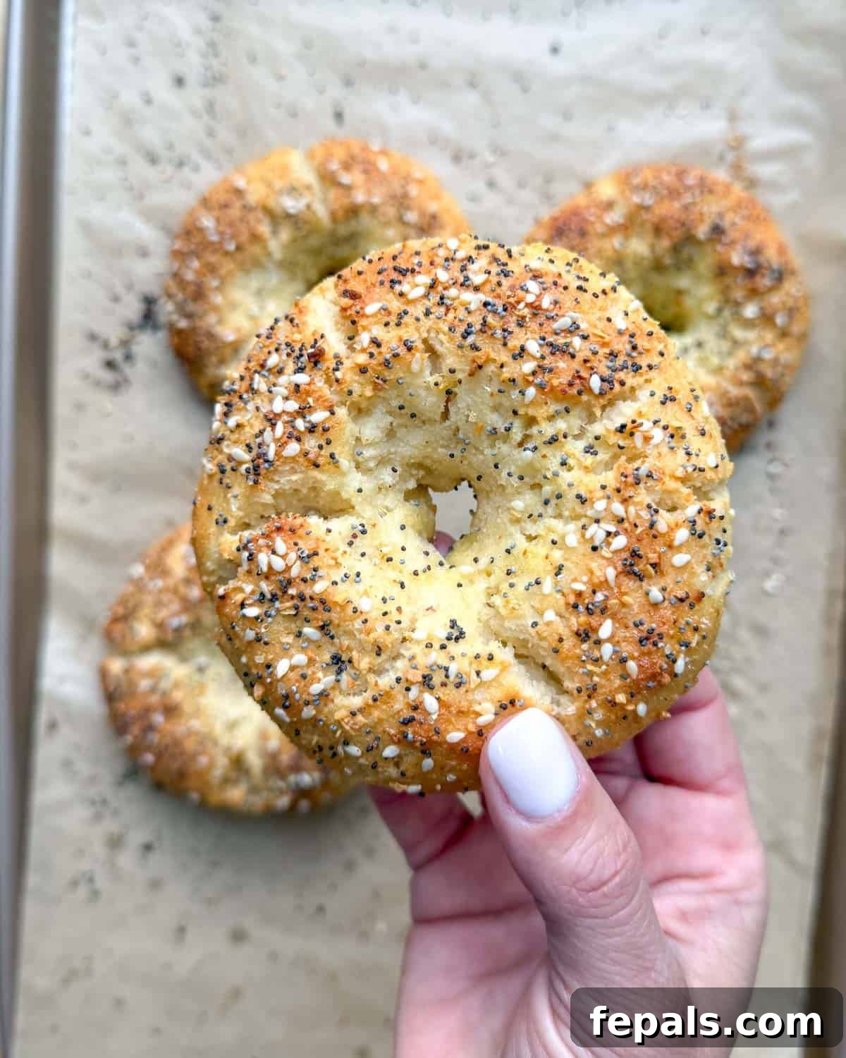Low-Carb Almond Bagels 12 A hand holding up a single golden-brown almond flour bagel, ready to be enjoyed.