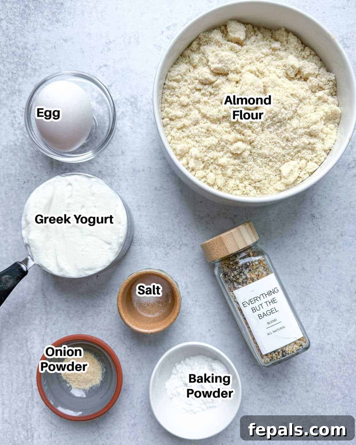 Low-Carb Almond Bagels 3 A flat lay photograph displaying the simple ingredients needed to make almond flour bagels, including almond flour, Greek yogurt, egg, and seasonings.