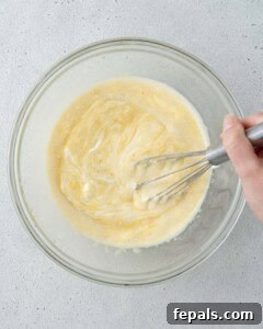 Wet ingredients and yogurt being mixed together with a whisk in a glass bowl.