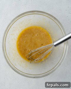 Eggs, sugar, and vanilla extract whisked together in a glass bowl with a whisk in it.