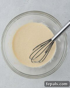 Whisking wet ingredients including yogurt, eggs, vanilla, milk, and sugar in a glass bowl.