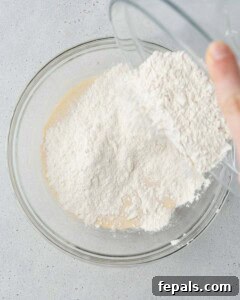 Flour being added to the wet ingredients in a glass mixing bowl.