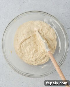 Muffin batter being gently mixed with a spatula in a glass bowl.