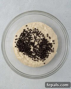 Glass bowl filled with muffin batter topped with mini chocolate chips, ready to be folded in