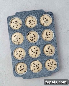 Muffin tin filled with raw batter, each cup topped with a few chocolate chips before baking.