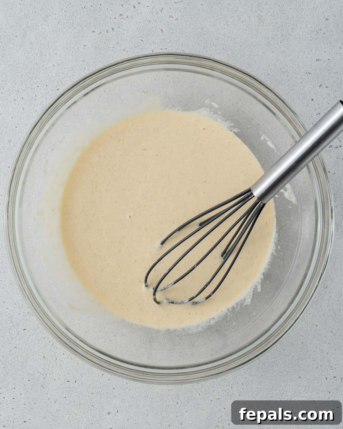 Whisking wet ingredients including yogurt, eggs, vanilla, milk, and sugar in a glass bowl.
