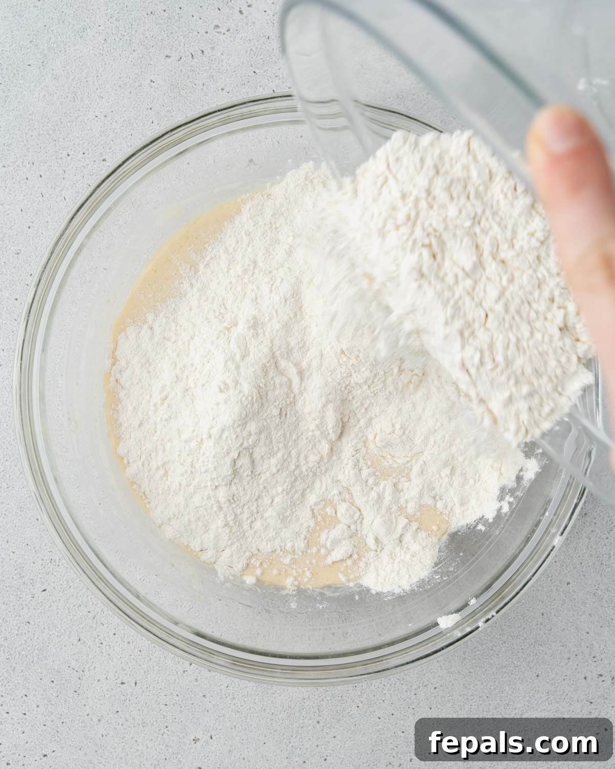 Flour being added to the wet ingredients in a glass mixing bowl.