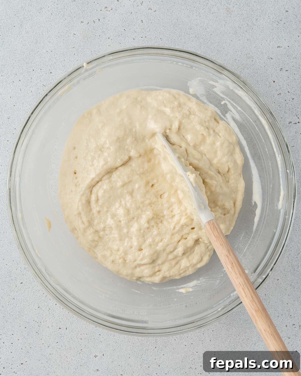 Muffin batter being gently mixed with a spatula in a glass bowl.