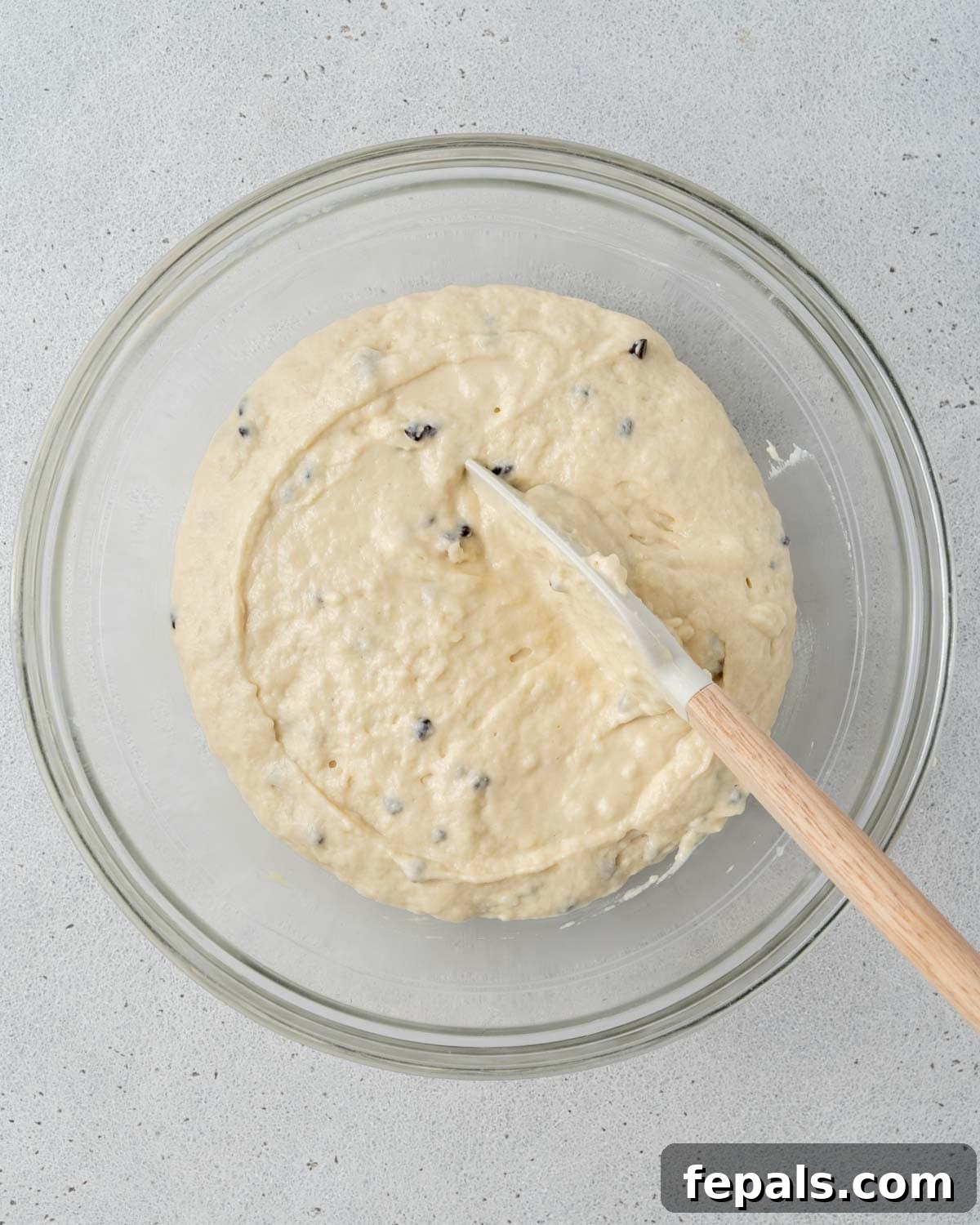 Top view of glass bowl with muffin batter being mixed with chocolate chips in it.