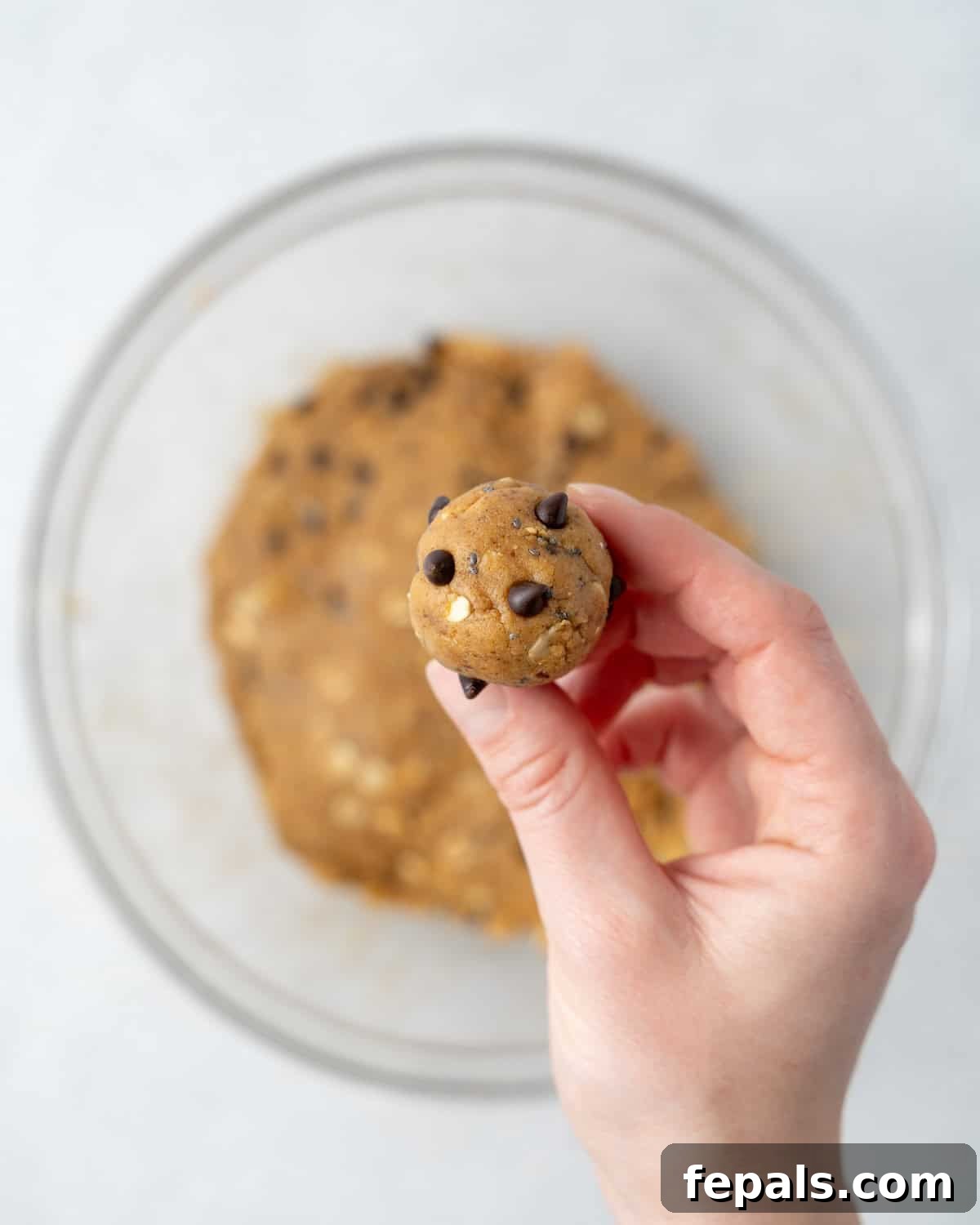 A hand holding a single peanut butter snack ball, showcasing its perfect round shape.
