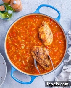 Pan of simmering tomato sauce with chicken breasts being added in with tongs.