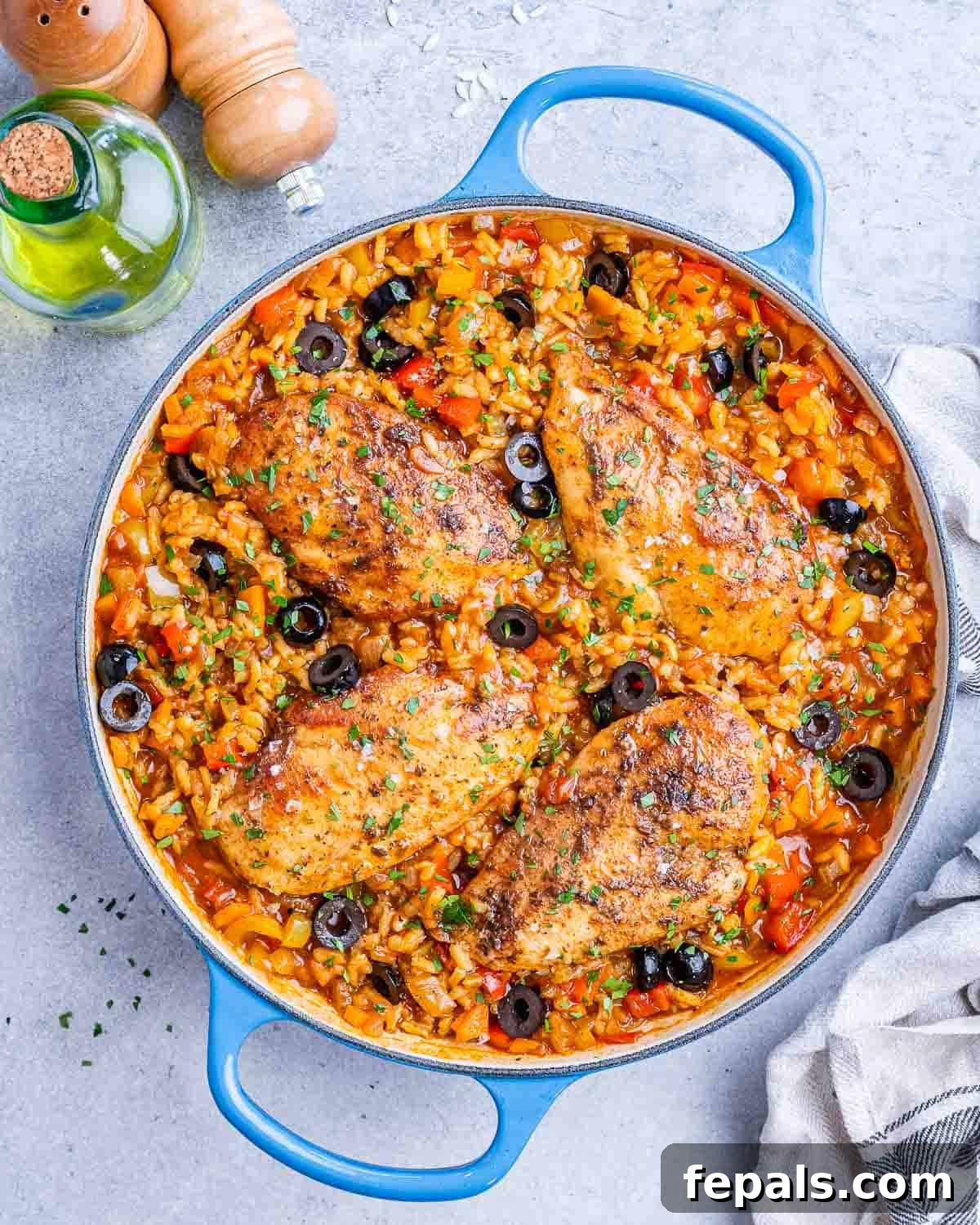 Skillet of cooked Spanish chicken and rice, topped with sliced black olives and fresh parsley, ready to serve.