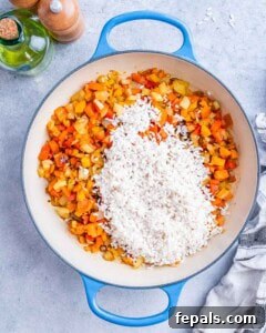Rice added to sautéed vegetables in a skillet, ready to be stirred and toasted.