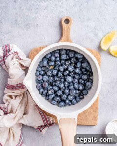 White saucepan filled with fresh blueberries sitting on a wooden board, ready to be cooked down for compote.