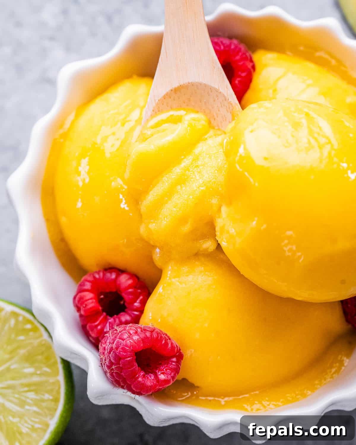 Tropical Mango Sorbet 2 A bowl with three scoops of vibrant mango sorbet, elegantly topped with fresh raspberries, hinting at its refreshing and delicious taste.