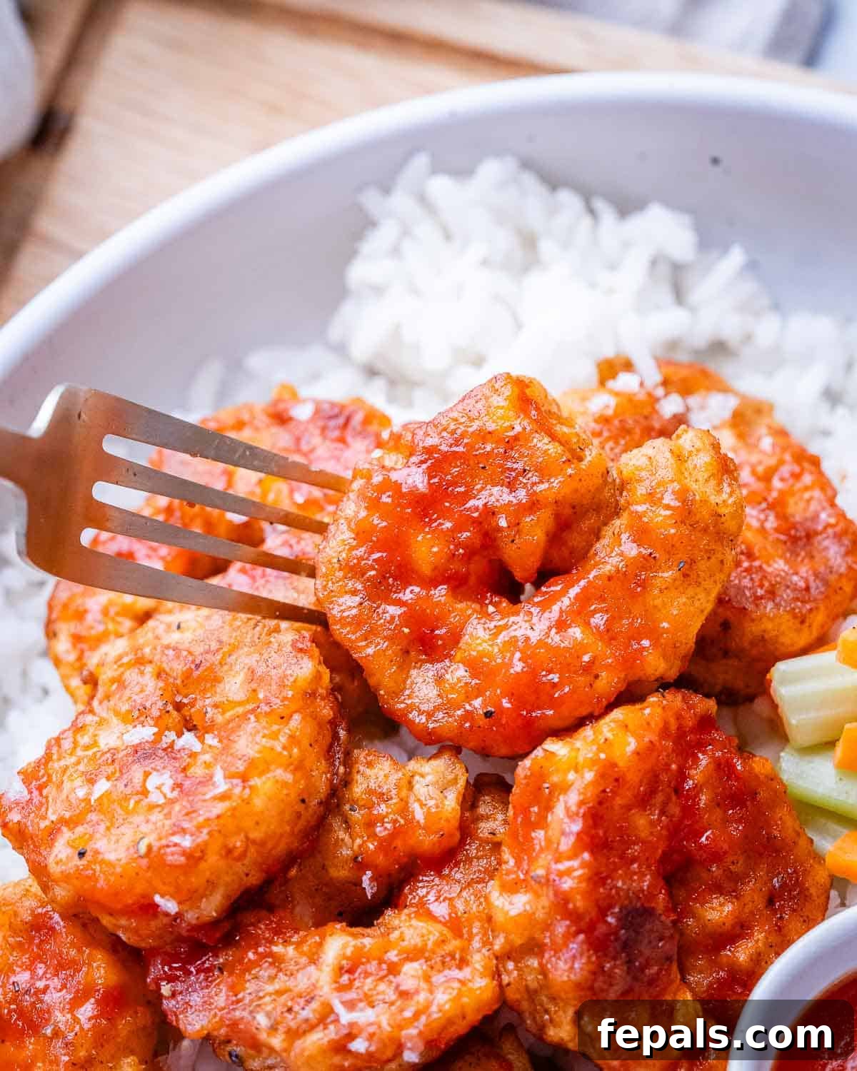 A closeup of buffalo shrimp on a fork, showcasing its crispy texture and vibrant sauce.