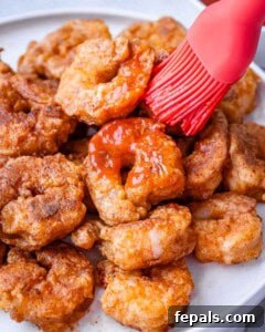 Cooked buffalo shrimp being basted with sauce in a serving bowl.