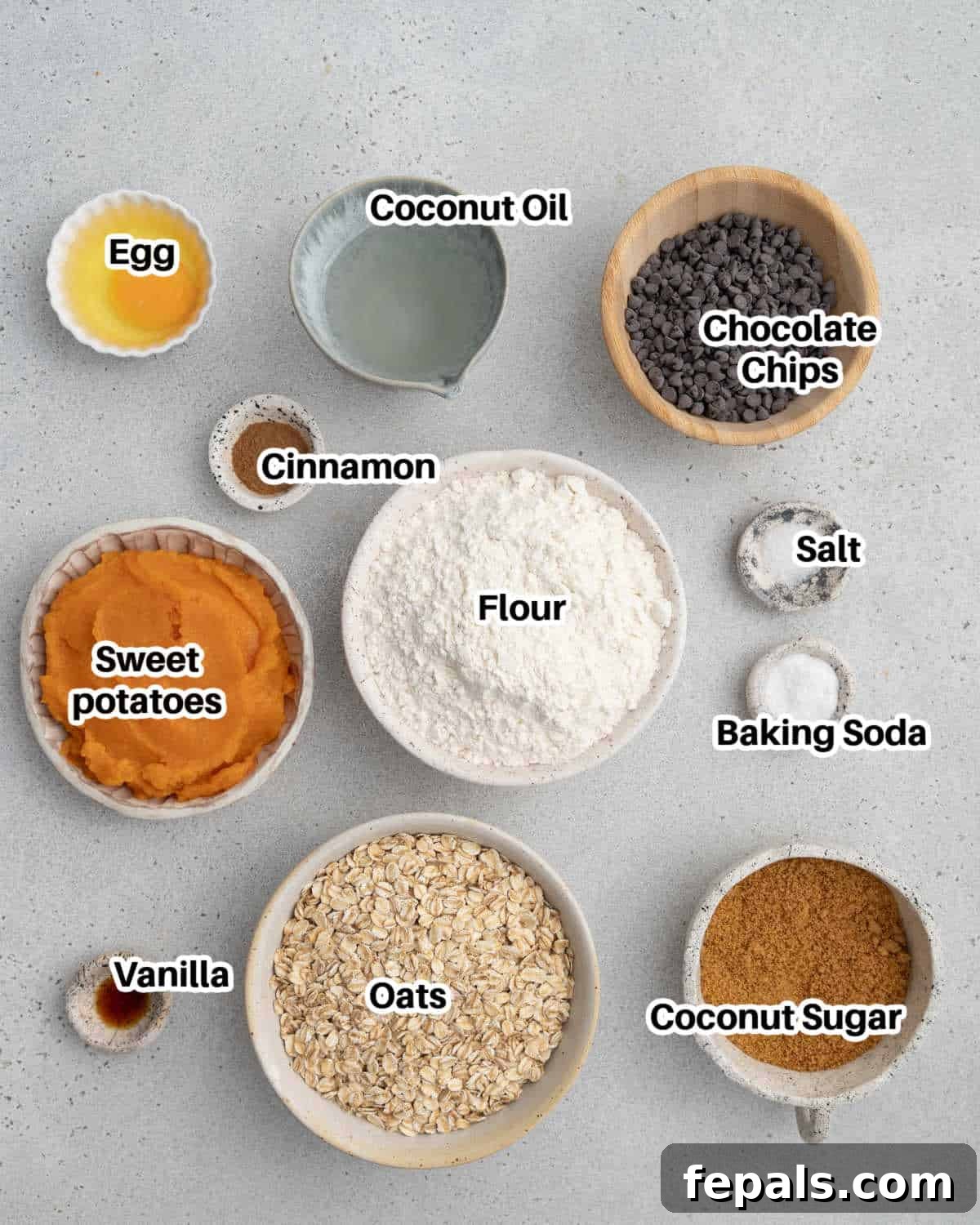 A collection of fresh ingredients laid out, including sweet potatoes, oats, flour, chocolate chips, and spices, ready for baking sweet potato cookies.