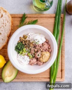 Ingredients for tuna mixture in a bowl before mixing: tuna, yogurt, mustard, mayonnaise, lemon juice, dill, and capers.