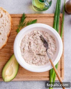Bowl of tuna mousse mixture on a wooden board with fresh avocado, bread, and dill alongside.