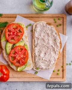 Open sandwich showing layered avocado slices and tomato slices with seasoning, ready to be closed.