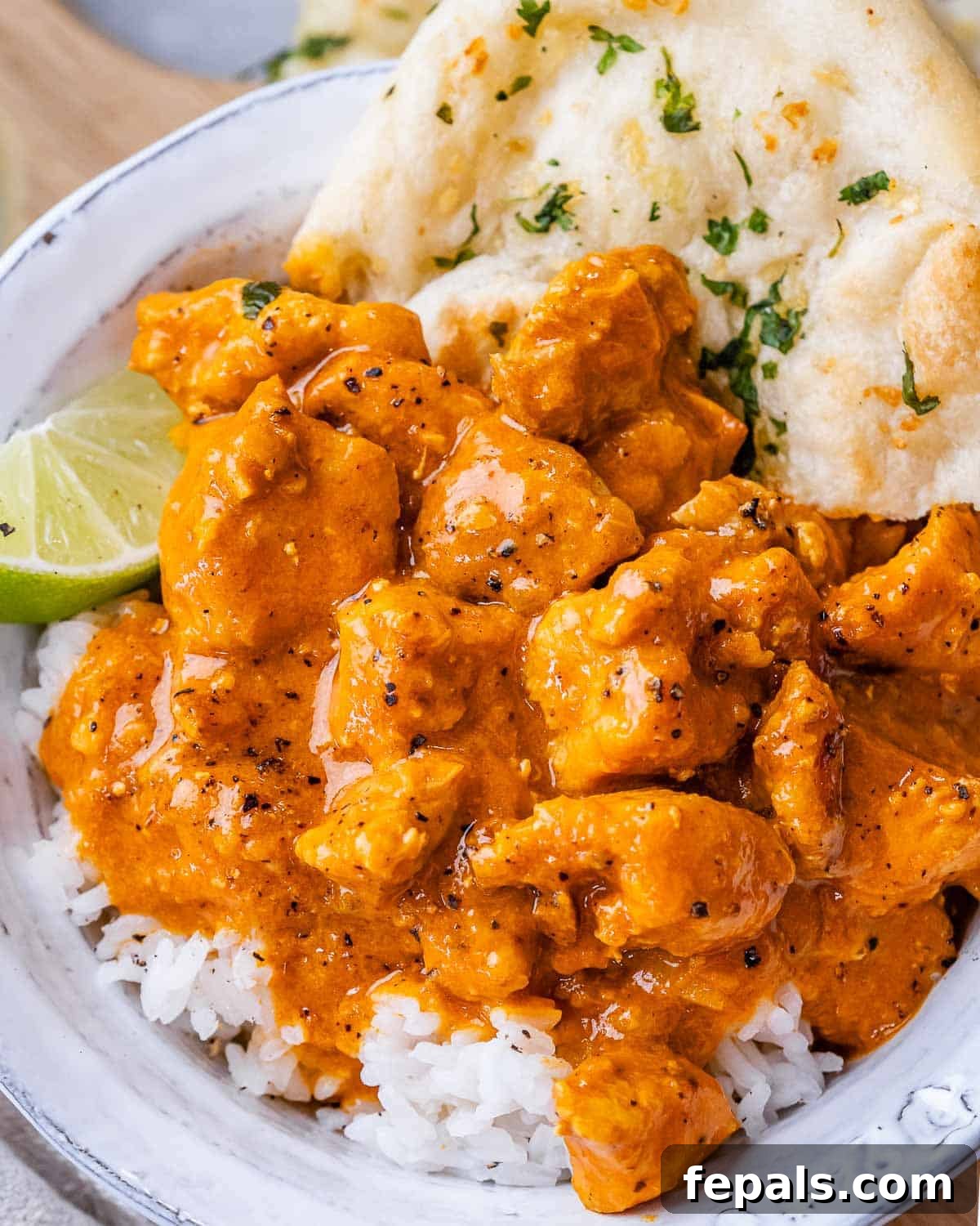 A bowl of slow cooker chicken curry with rice and a side of naan bread, garnished with fresh cilantro.