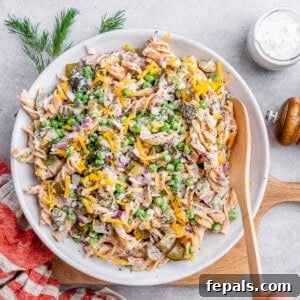 Wooden spoon stirring a large white bowl of dill pickle pasta salad, showing a well-mixed creamy texture.