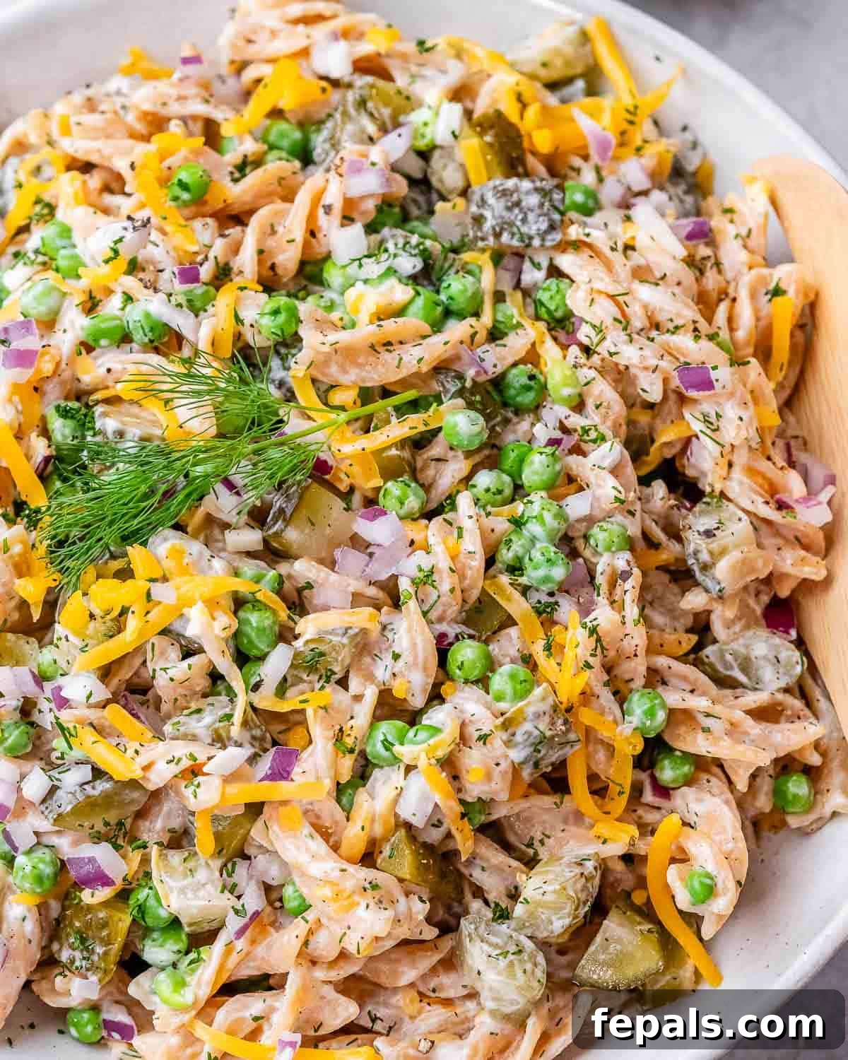 Overhead view of dill pickle pasta salad, highlighting texture and color from red onion, cheese, and peas.