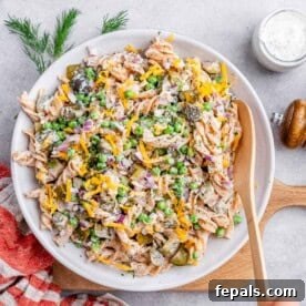 Wooden spoon stirring a large white bowl of dill pickle pasta salad, showing a well-mixed creamy texture.