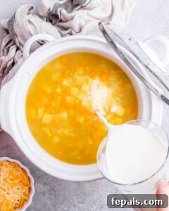 Milk being poured into the crockpot filled with broth, potatoes, carrots, and celery.