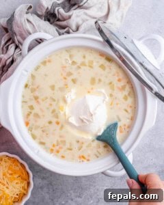 A scoop of cream cheese being added to the slow cooker with the cooked soup base.