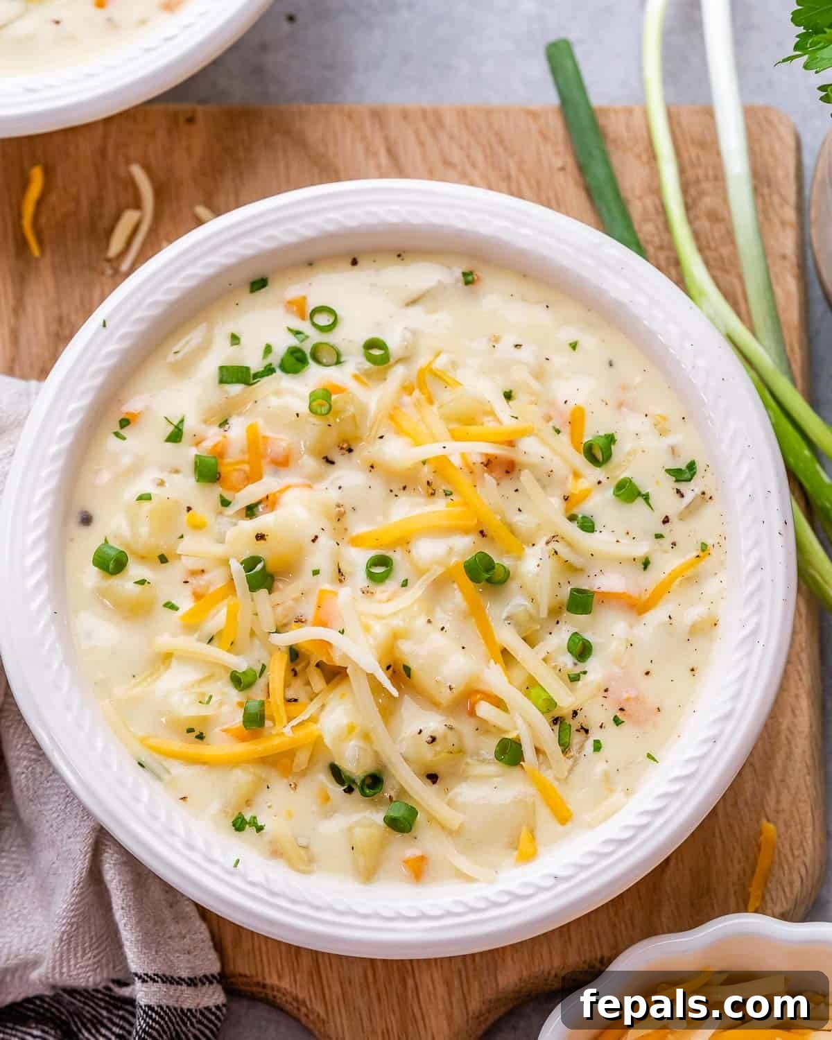A bowl of potato soup topped with shredded cheddar cheese and sliced green onions.