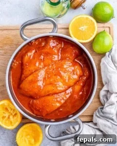 Chicken breasts marinating in a bowl of bright orange-red achiote citrus marinade.